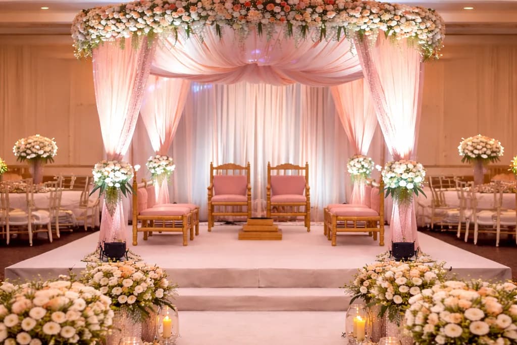 Blush pink floral stage with draped canopy, gold chairs and white flower arrangements