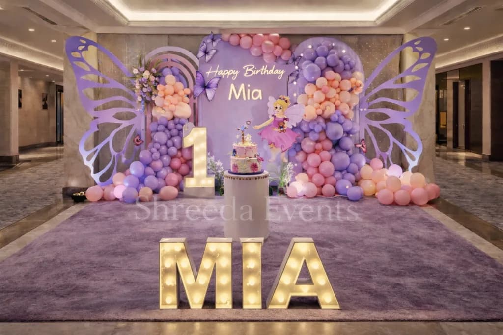 Lavender butterfly backdrop with balloon clusters, a number one and light-up name letters