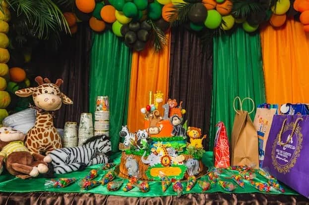 Jungle safari birthday table with green and orange drapes, a balloon garland and plush safari animals