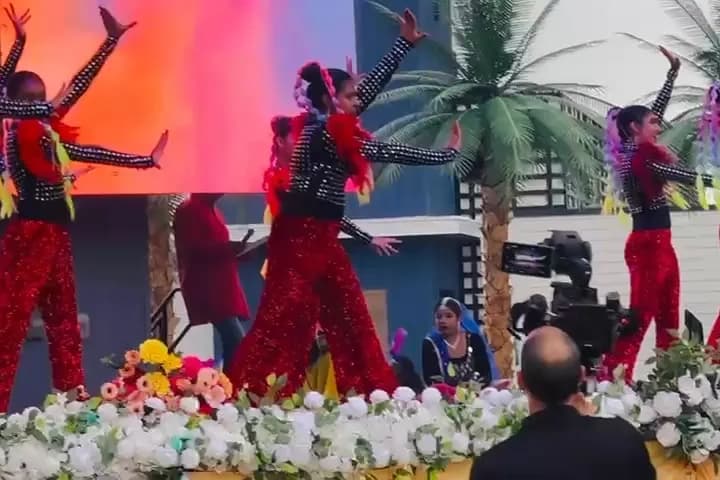 Dancers in red performing on a stage edged with white and red flowers, with palm tree props at the side