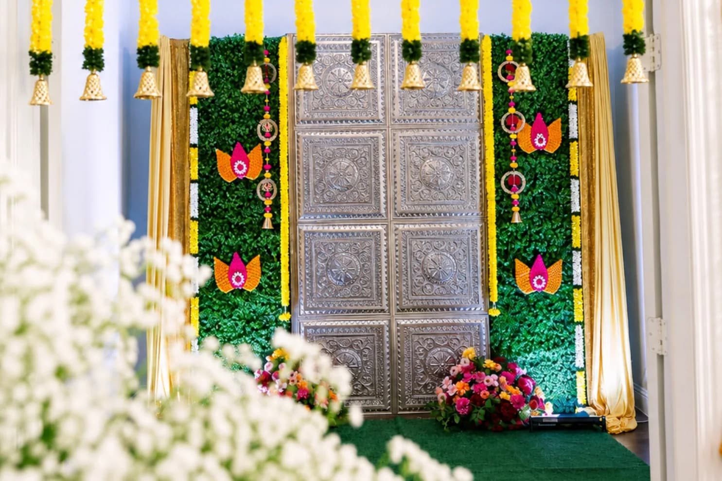 Front door framed by a green foliage wall, gold drapes, lotus panels and hanging marigold strings, with baby's breath in the foreground
