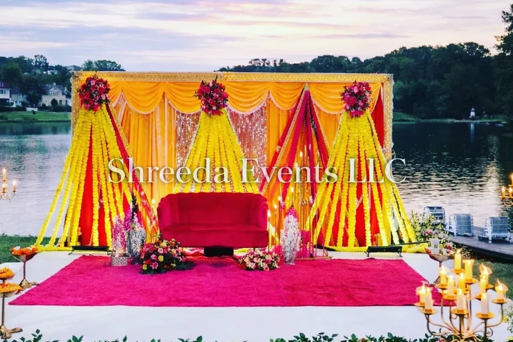 Lakeside stage with yellow and orange drapes, a red seat, a pink carpet and a border of flowers beside the water