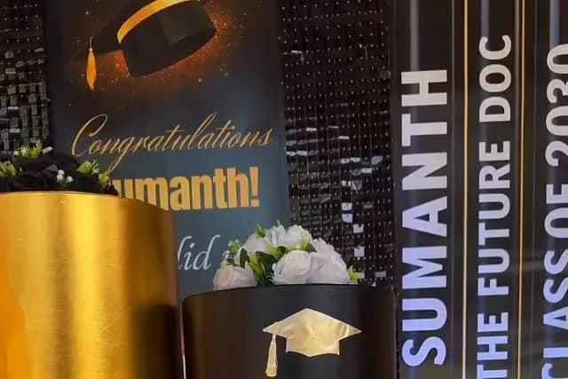 Black sequin graduation backdrop with a Congratulations Sumanth sign, gold and black plinths with white flowers, and a The Future Doc Class of 2030 banner