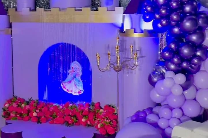 Lavender castle backdrop with a lit arched window, purple and white balloon clusters and a border of red and pink flowers