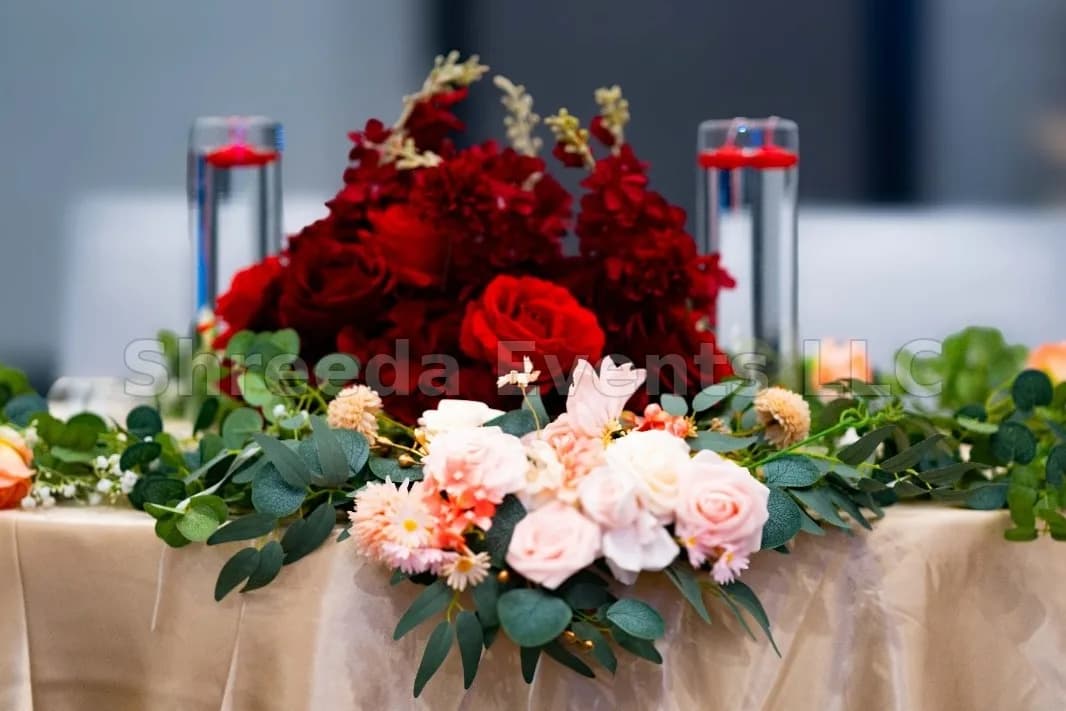 Low floral centerpiece of red roses, blush blooms and greenery on a gold tablecloth