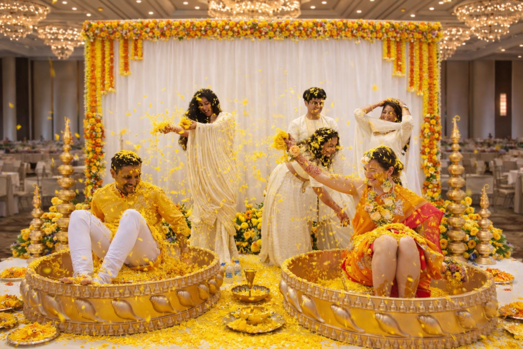 Haldi ceremony decoration with marigold backdrop, white stage draping, brass seating bowls, and floral petals celebration by Shreeda Events in Dallas DFW