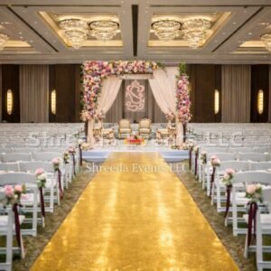 Luxury indoor wedding mandap with pink floral arch and royal shiny golden carpet aisle in a large ballroom by Shreeda Events